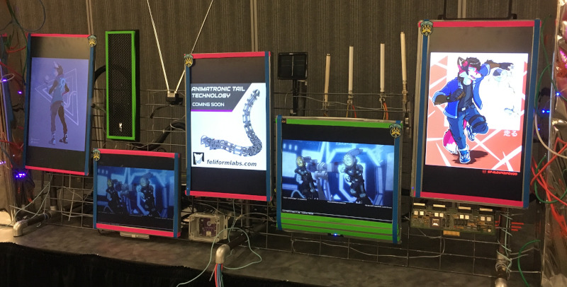 Several computer monitors, one showing an advertisement for the Feliform Labs tail technology